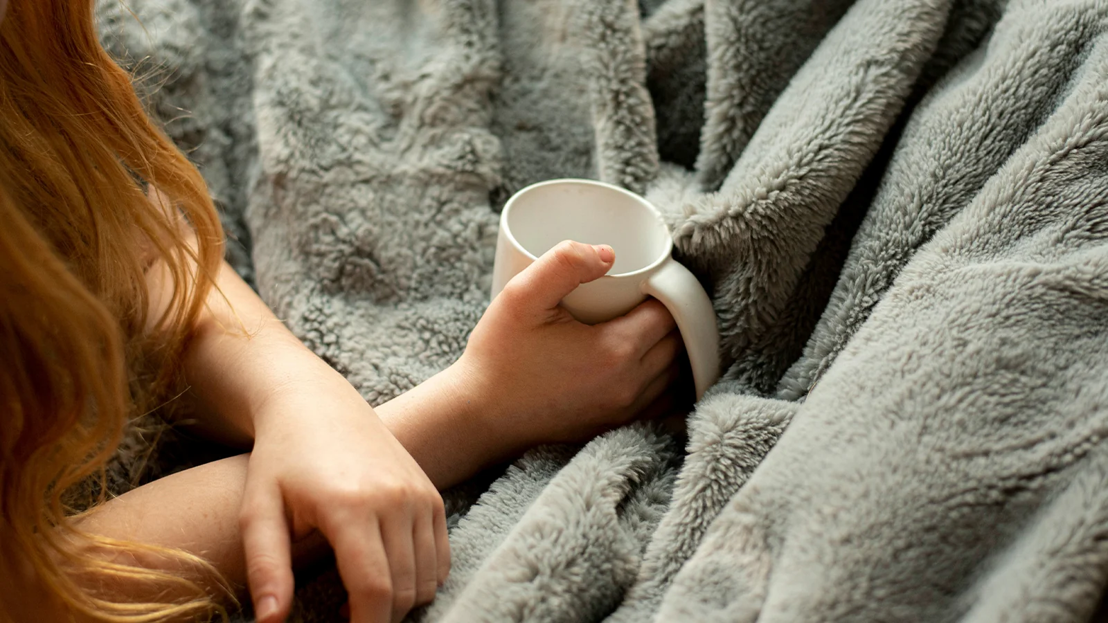 ブランケットを膝にかけてコーヒーを飲んでいる女性